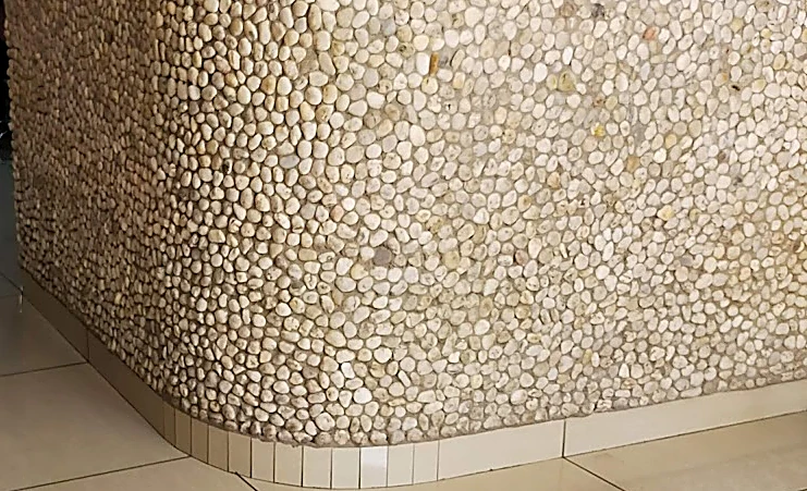 Curva del mostrador de recepción cubierto de canto rodado claro, sobre piso de loseta beige